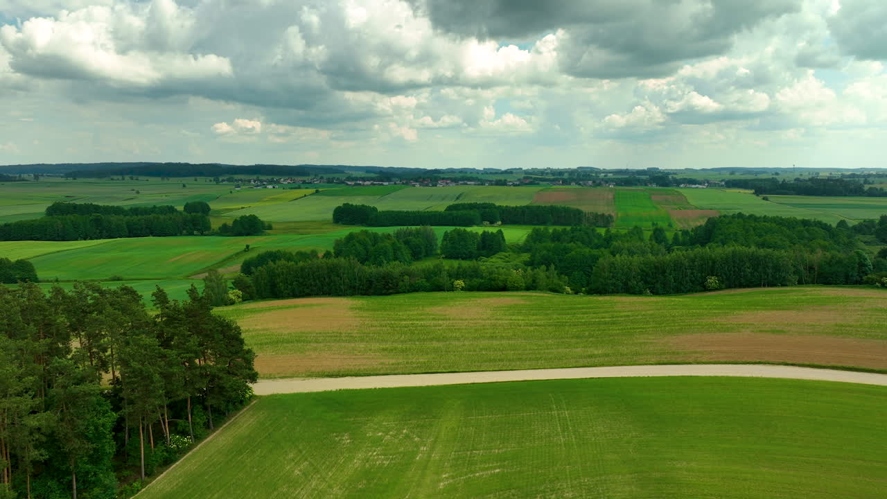 Aerial footage showing expansive green fields and patches of trees under a partly cloudy sky