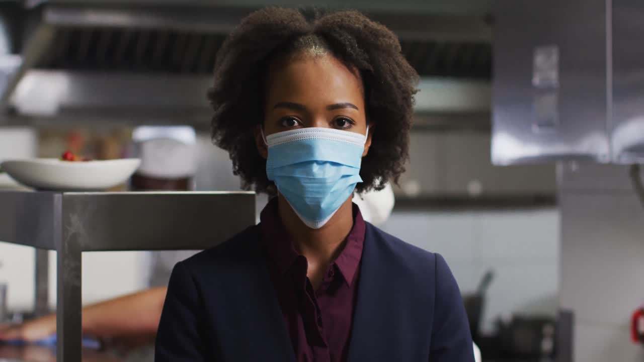 Portrait of african american female manager wearing face mask in restaurant kitchen