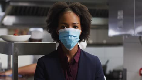 portrait of african american female manager wearing face mask in restaurant kitchen