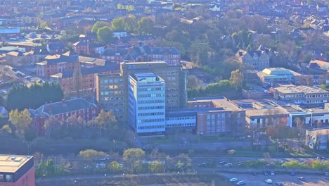 drone view above chesterfield college, england, capturing its architecture nestled within an autumn landscape, urban greenery and flowing morning traffic through the cityscape.