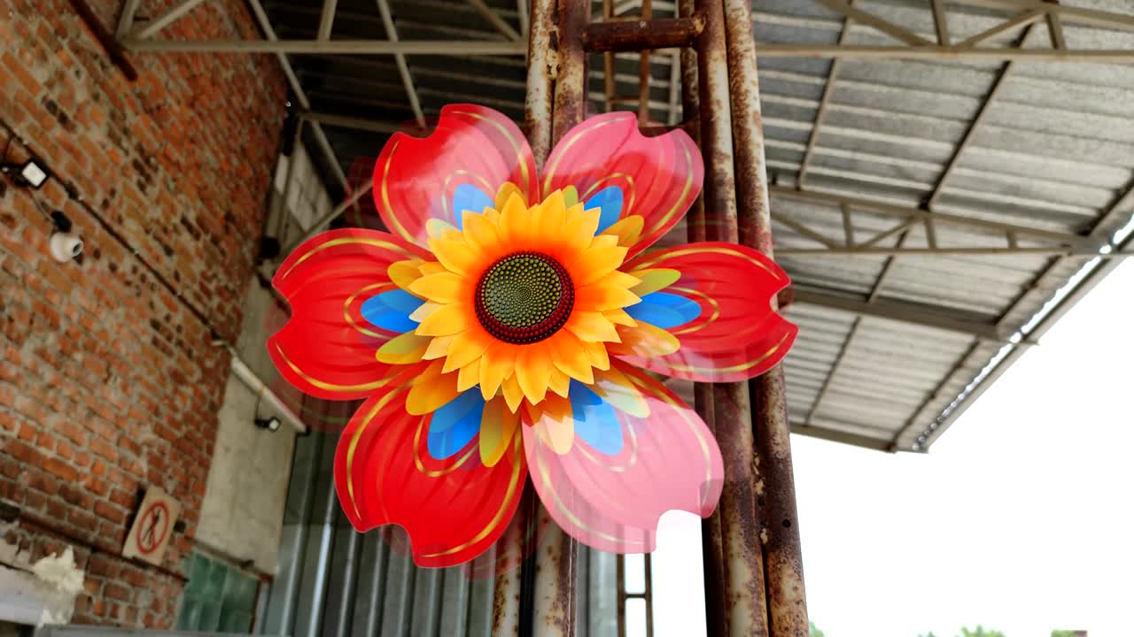 Toy windmill in the shape of a sunflower on the industrial bulding background. Concept alternative energy.