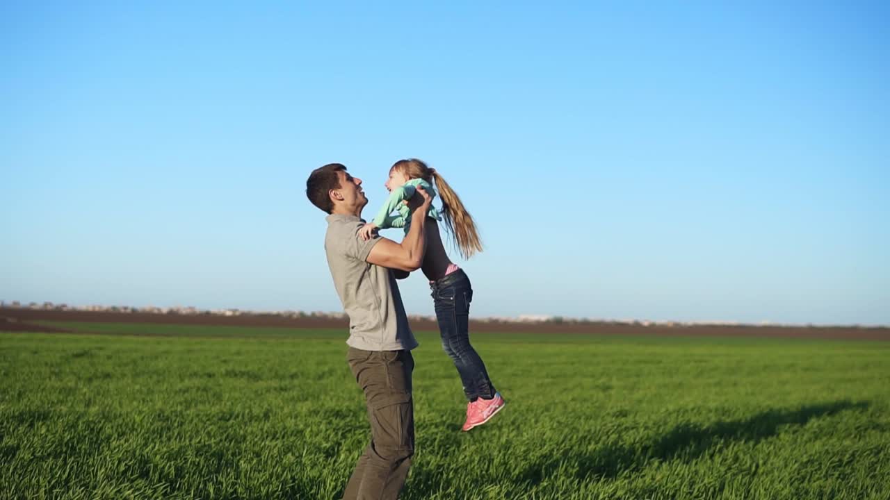 Slow motion of handsome young father throwing his adorable daughter in the air. Active life. Beautiful green field