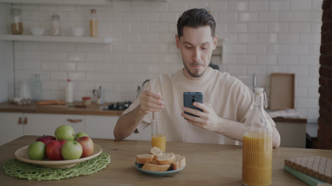 Man having breakfast in the kitchen and using his phone
