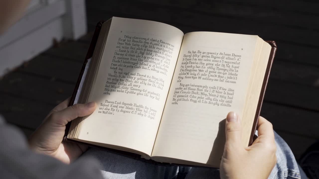 Sun shifting, reader adjusting hands holding open hardback book on porch over jeans, reducing glare