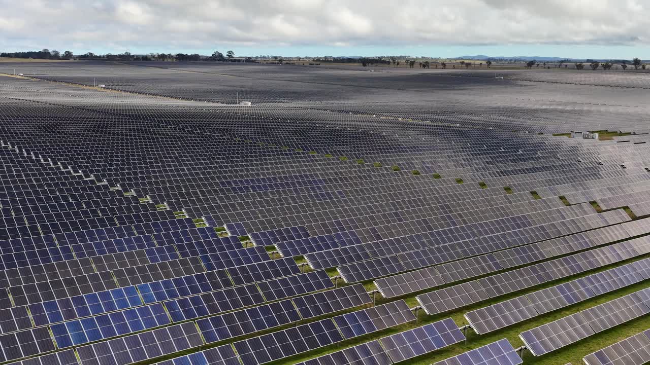 Wide aerial pan reveals extensive solar panel array under cloudy sky, emphasizing renewable energy landscape
