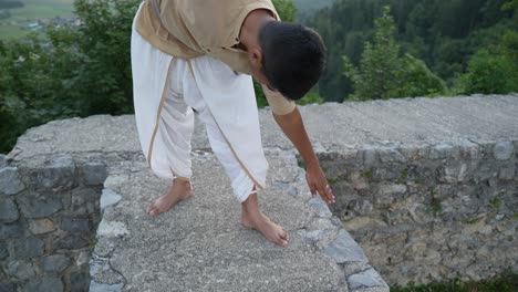 eyes-closed indian man doing meditation in the morning at hill top with sunrise in the background on stone wall of castle ruins