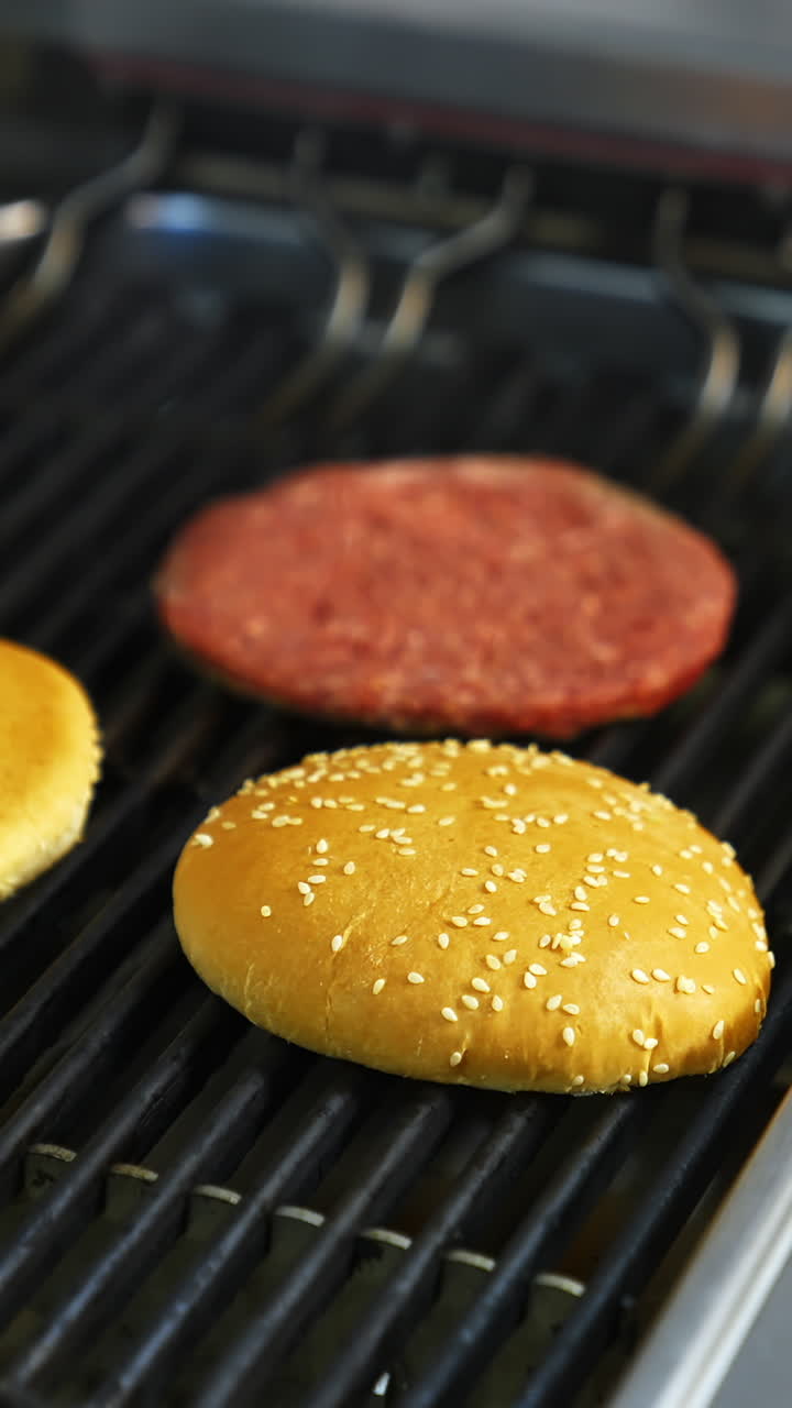 Fresh buns and raw cutlet are grilled on a barbeque. Selective focus on frying process. Vertical video
