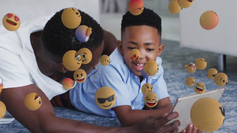 animation of emoticons over happy african american father and son using tablet
