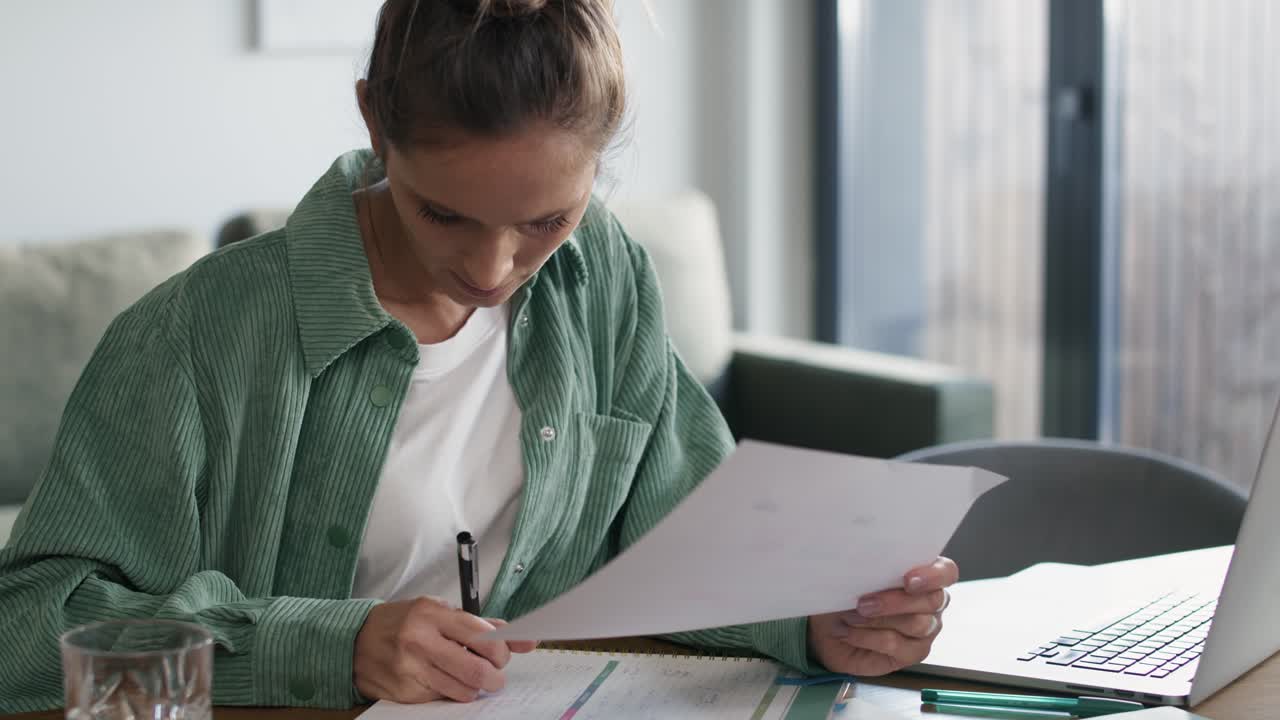 Caucasian woman working on computer and making notes at home