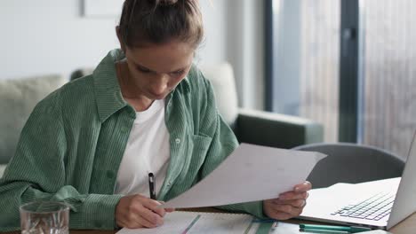 caucasian woman working on computer and making notes at home