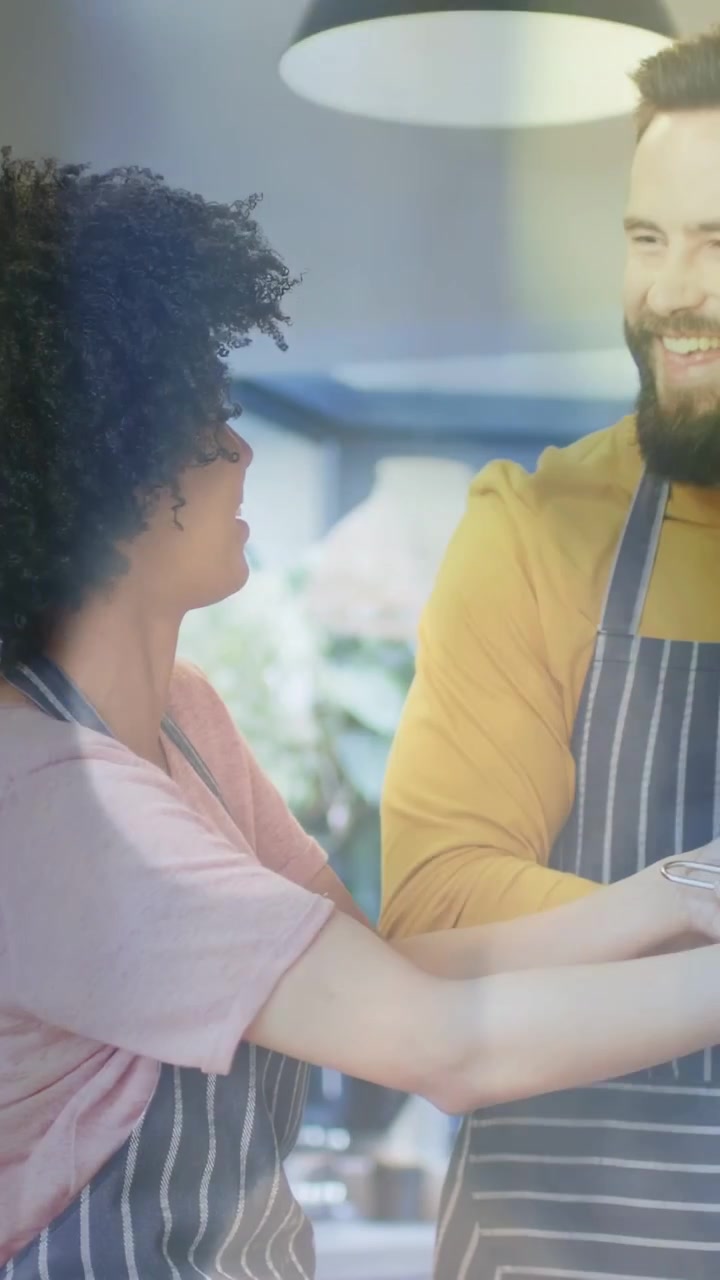 Video verticale: Donna che si protende verso il partner che tiene una ciotola, cucinando, toccandosi il viso, sorridendo vicino a una lampada