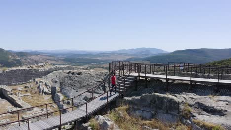 Eine-Drohnenaufnahme-Aus-Der-Umlaufbahn-Zeigt-Einen-Mann,-Der-über-Eine-Rampe-Aus-Holzbrettern-Auf-Der-Spitze-Der-Antiken-Stadt-Perperikon-In-Der-Provinz-Kardschali-In-Bulgarien-Zu-Einem-Wasserreservoir-Läuft.