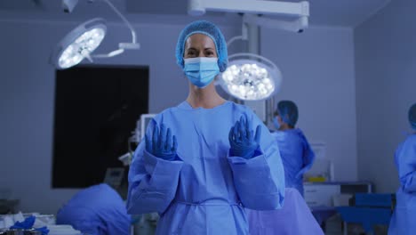 Portrait-of-caucasian-female-surgeon-wearing-face-mask-and-protective-clothing-in-operating-theatre