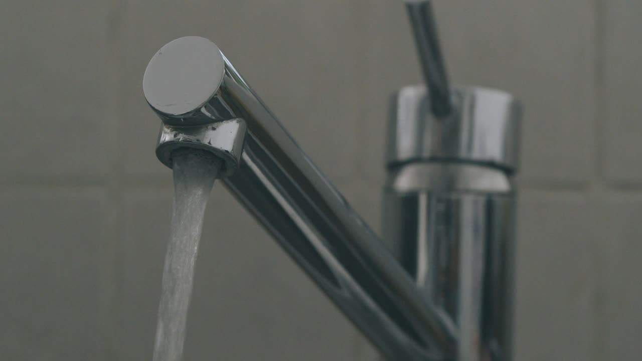A hand opens a sink faucet and lets out water in slow motion