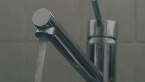 a hand opens a sink faucet and lets out water in slow motion