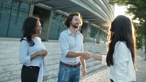 jovem empresário bem-sucedido apertando as mãos de uma parceira com assistente de negócios por perto