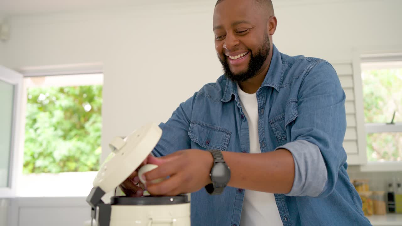 Uomo africano in jeans che tiene un uovo, lo rompe in una pentola e prepara contenitori per pasti su un'isola della cucina