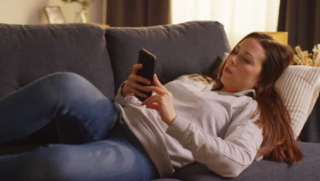 Primer-Plano-De-Una-Mujer-Tumbada-En-Un-Sofá-En-Casa-Viendo-Una-Película-O-Viendo-Una-Película-O-Navegando-Por-Internet-En-Un-Teléfono-Móvil-1