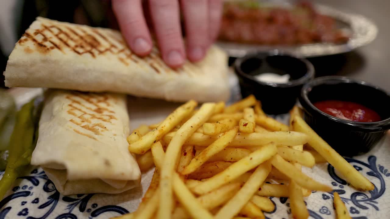 la mano alcanzando el kebab con papas fritas