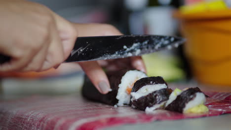slicing sushi roll with knife on kitchen counter, close-up