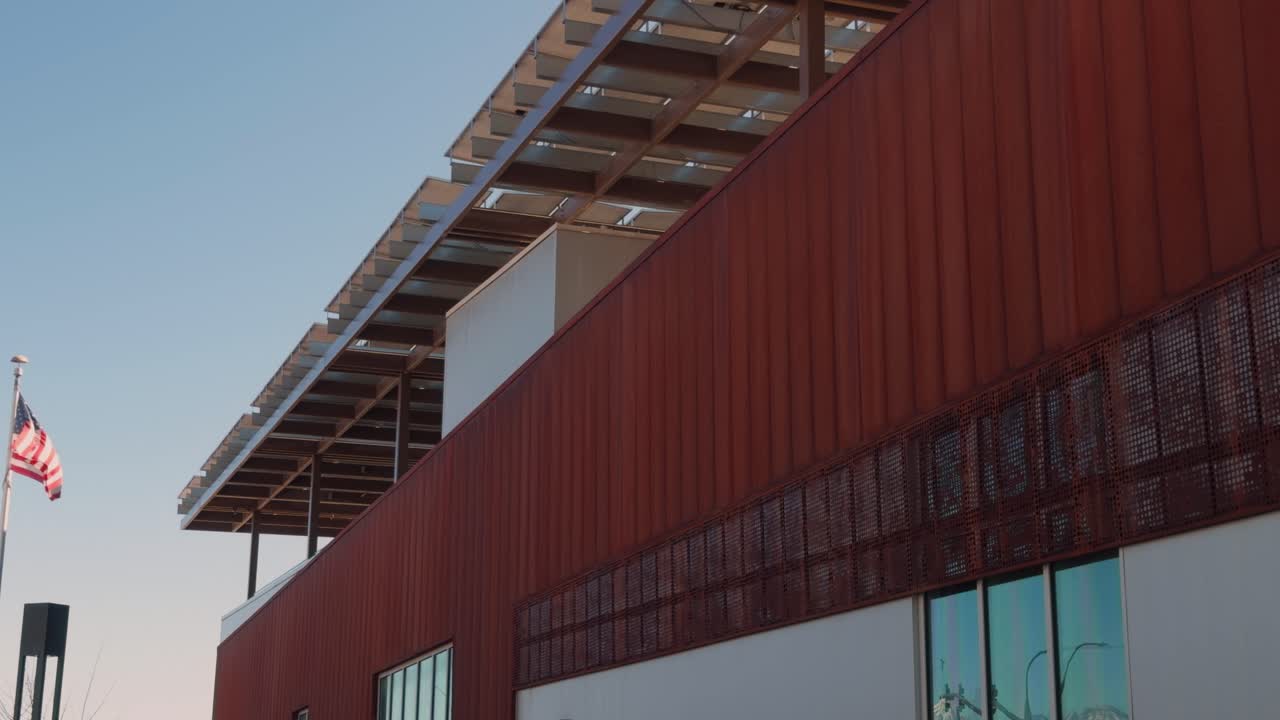 Lenta e costante panoramica da destra a sinistra della bandiera americana che sventola accanto all'esterno di un edificio moderno.