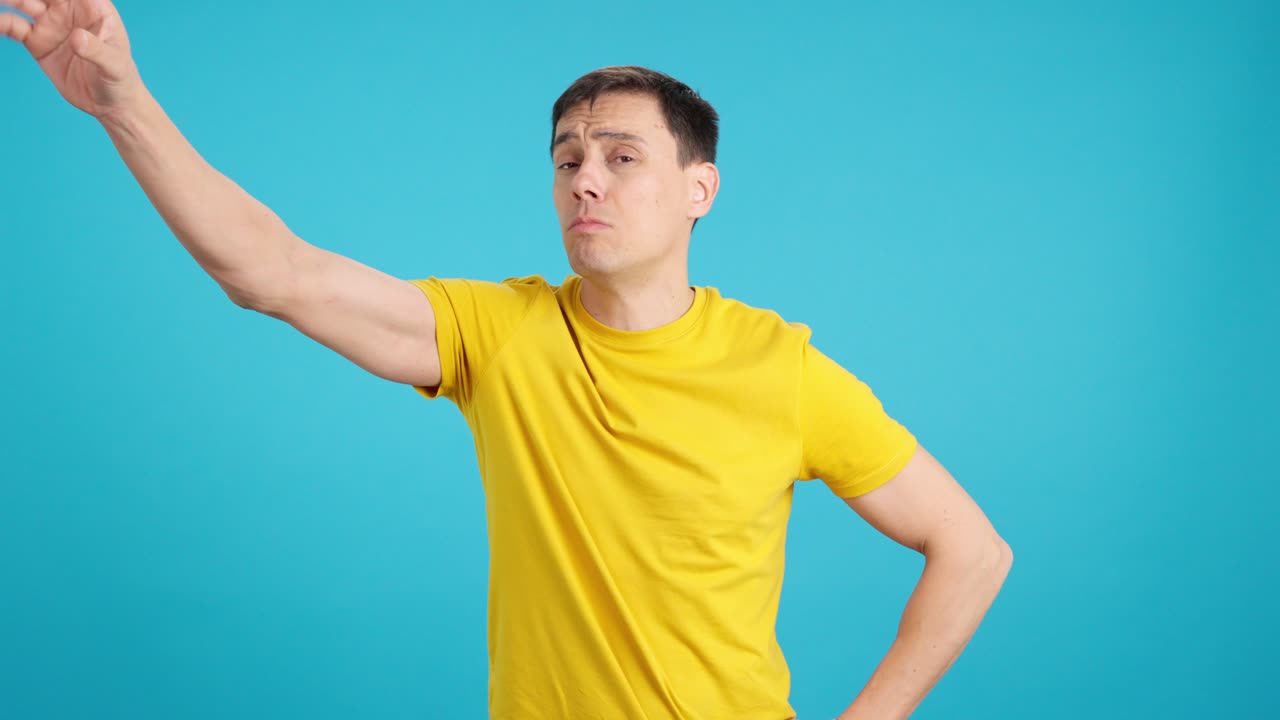 Man in yellow shirt making gestures on blue background