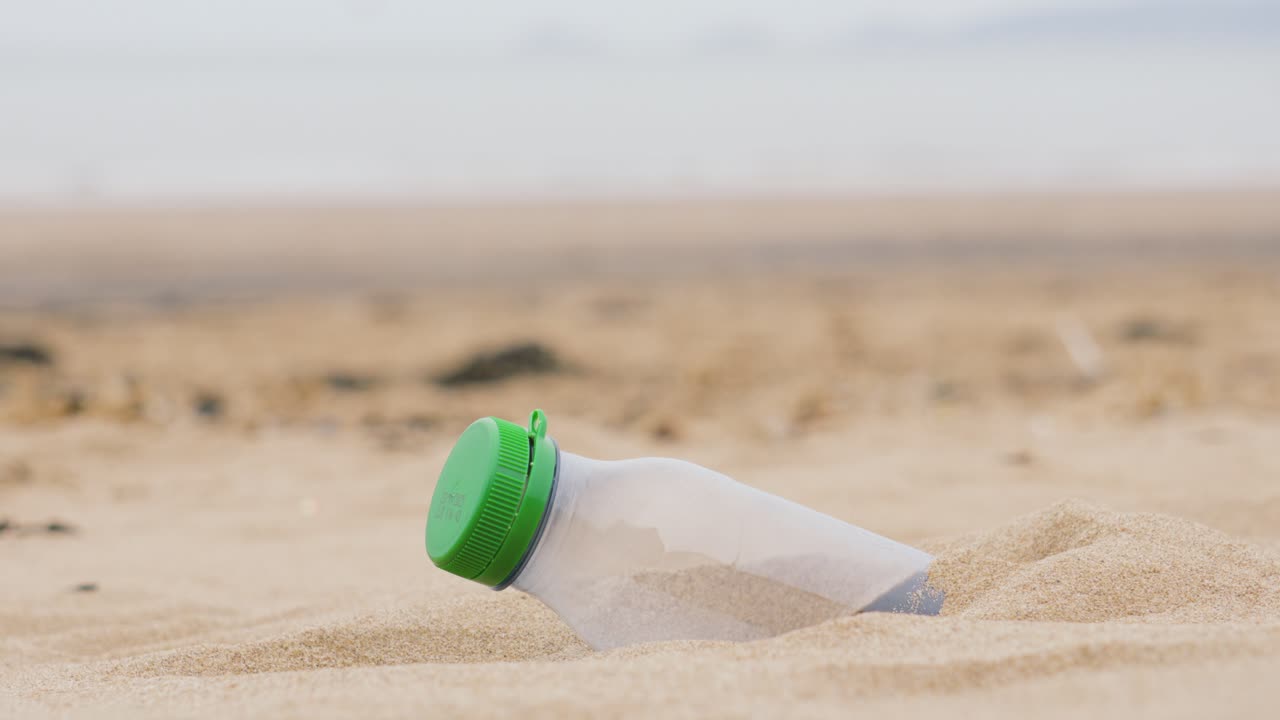 Static Shot of Plastic Bottle Partially Buried in Soft Sand with Sea in Background. Pollution of Natural Environment with Consumer Rubbish