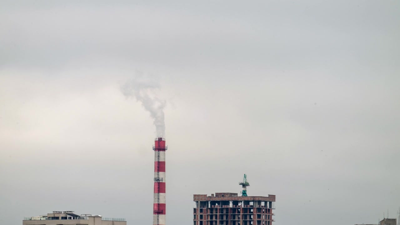 Time lapse of a striped industrial smokestack releasing steam above an urban skyline