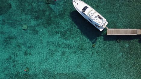 un yate blanco amarrado en un muelle de madera en el agua clara de la playa azul, el dron arriba hacia abajo