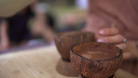 Unrecognizable-person-pouring-hot-cacao-from-thermos-into-coconut-shell-using-it-as-cups