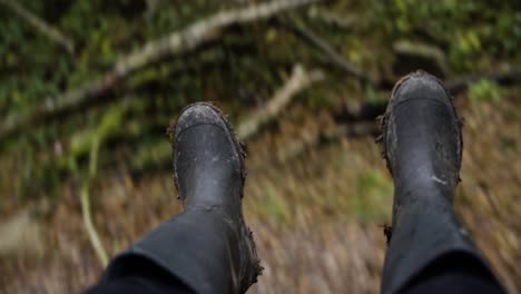 female feet in dirty rubber boots while swinging in the forest