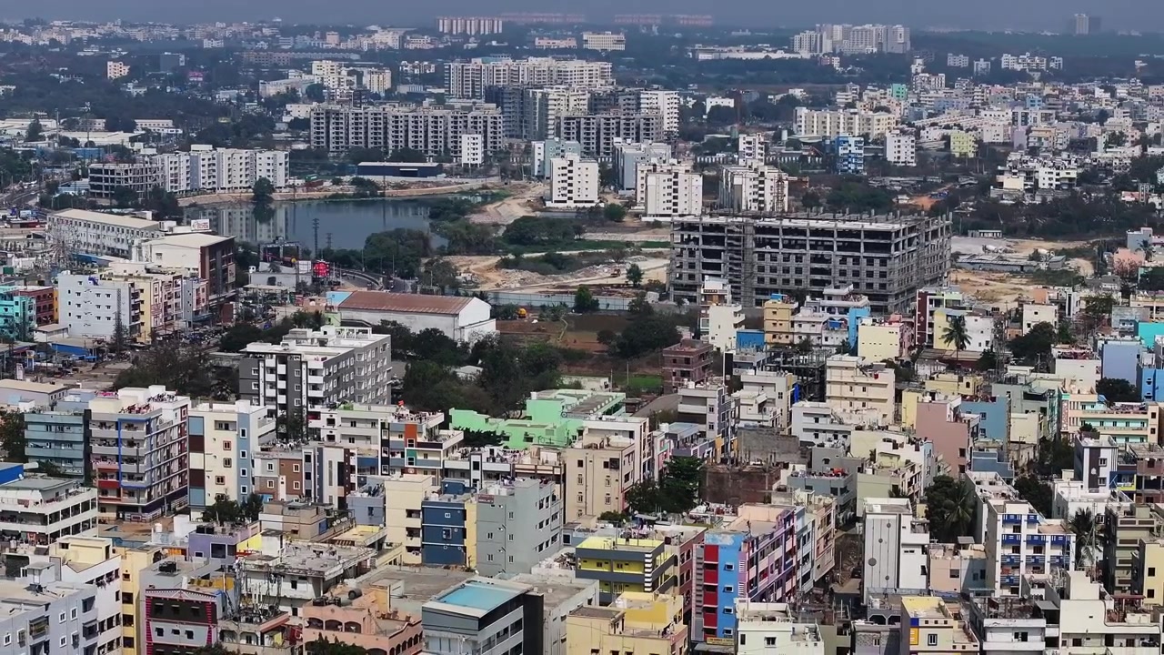 Edifici residenziali con appartamenti, Sri Sai Pooja Theatre, edificio in costruzione e il lago Kattamysamma a Suraram, Hyderabad, Telangana, India. Di giorno, ripresa a semicerchio, ripresa con drone, 4K.