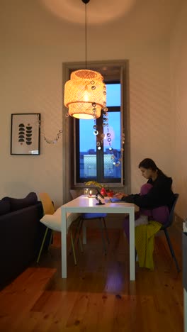 woman working at a table in a cozy dining room at night