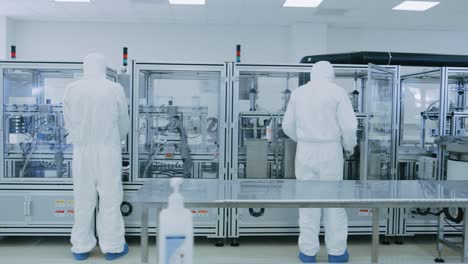 manufacturing laboratory where scientists in protective coverall's work with industrial high precision 3d printing machinery. manufacturing pharmaceutical / technological / industrial products.