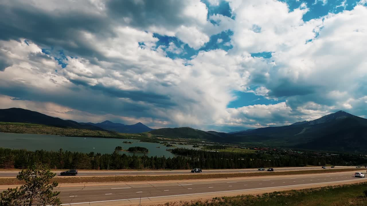 Timelapse fra stor højde, der fanger hurtig skybevægelse og flydende motorvejstrafik langs en naturskøn alpesø i Colorado Rockies