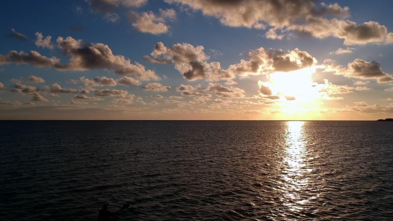 Silhouette of person kayaking in the ocean during sunset, aerial forward shot