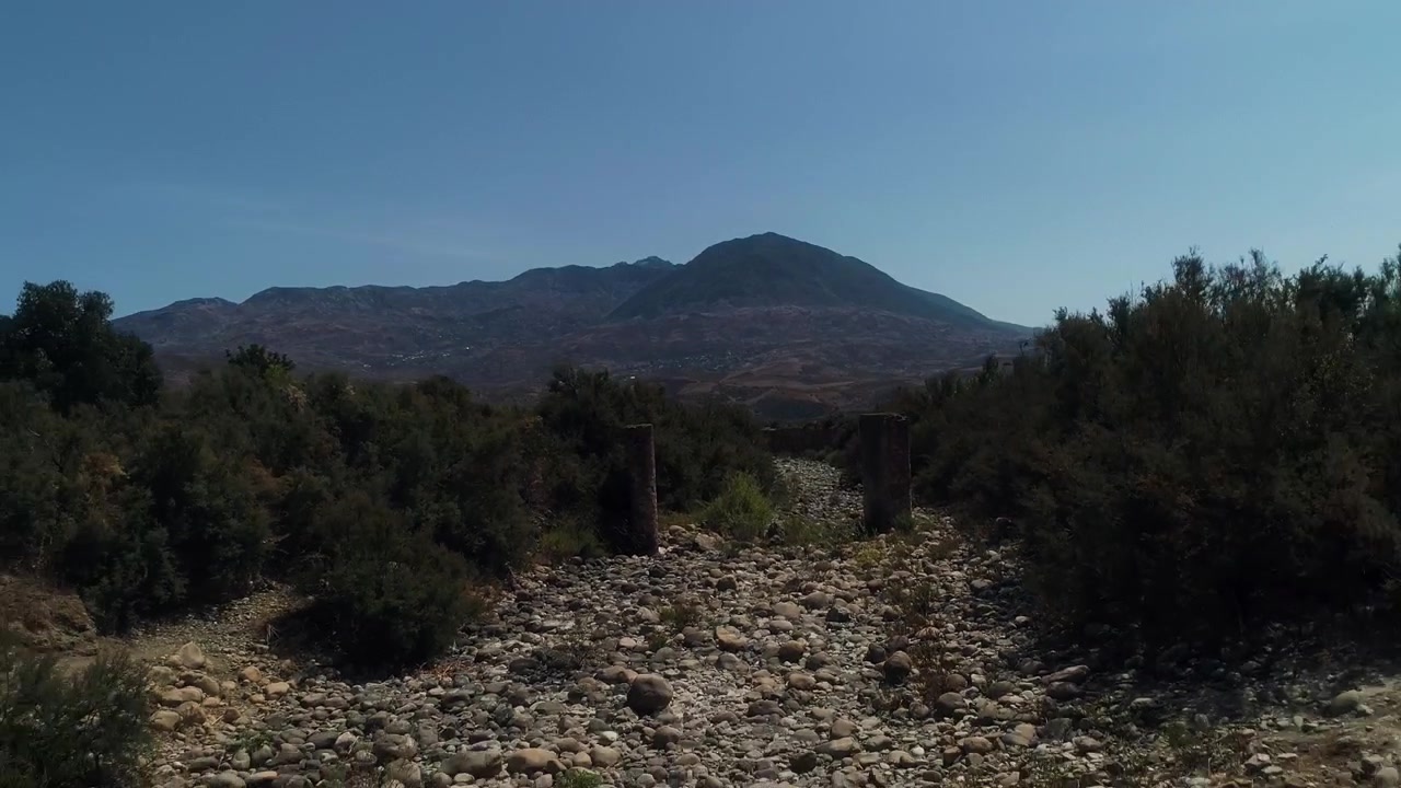 Il drone si allontana lungo un letto di fiume roccioso e asciutto verso aspre montagne in Marocco