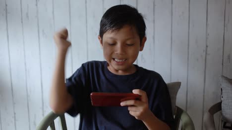 portrait of happy asian young boy enjoy success on mobile phone at home