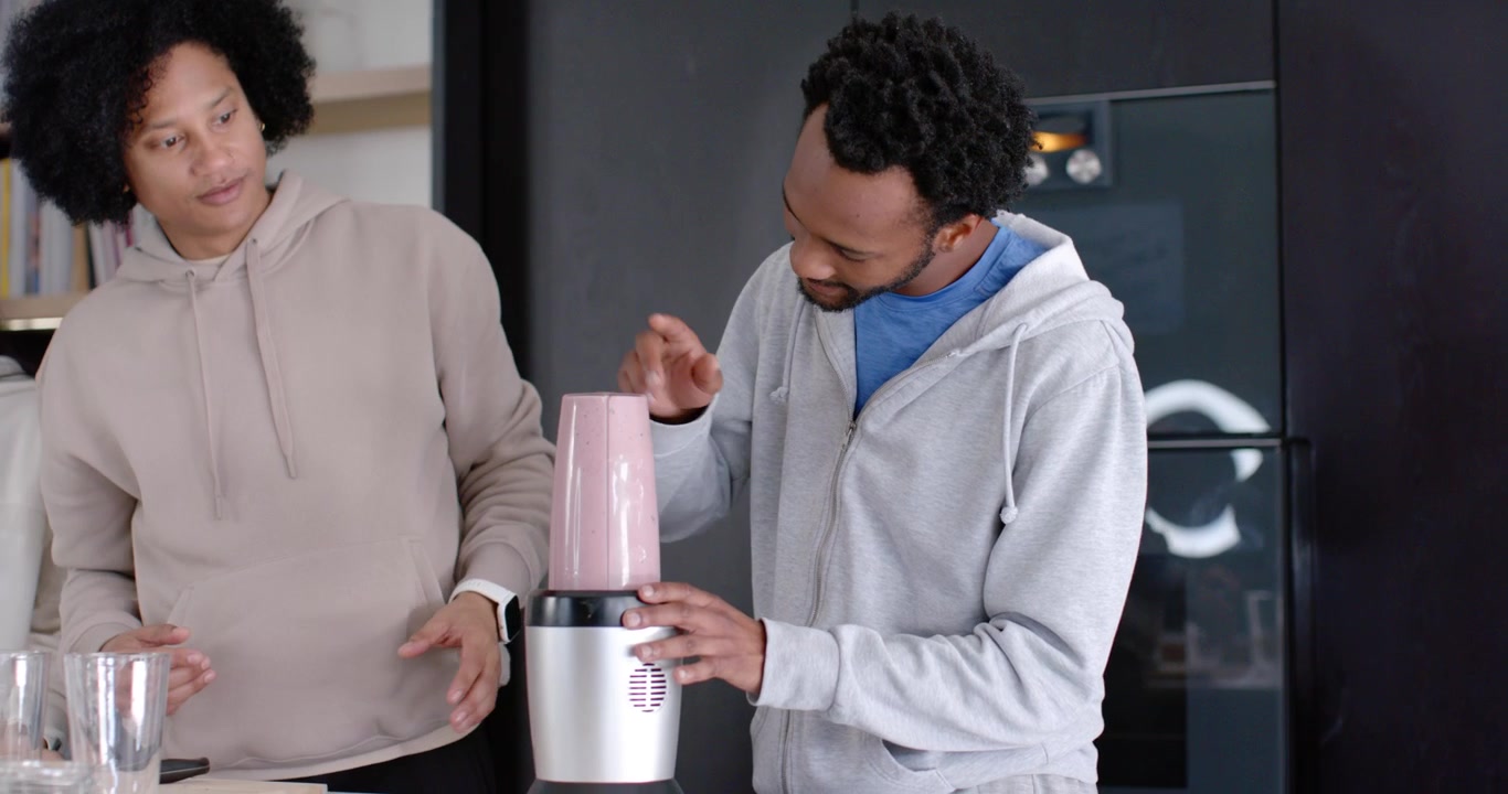 Diverse group in hoodies prepping glasses while right man plugging blender in kitchen for drinks