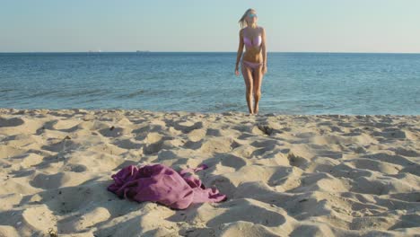 Beautiful-blonde-woman-in-a-bikini-walks-out-of-the-water-onto-the-beach-on-a-windy-day