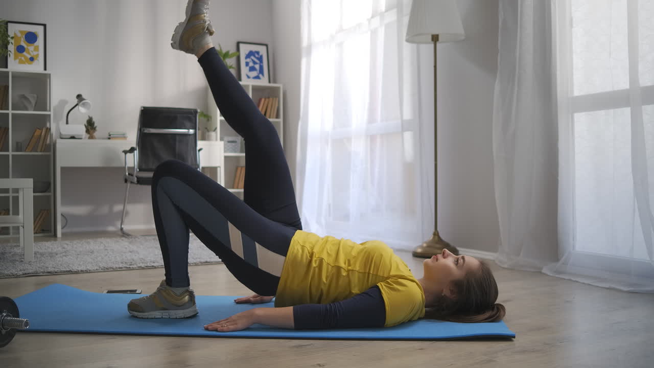 la mujer deportiva está haciendo ejercicio físico en casa acostada en el suelo y levantando la pierna y las caderas, perdiendo peso y manteniéndose en forma en el hogar durante el aislamiento