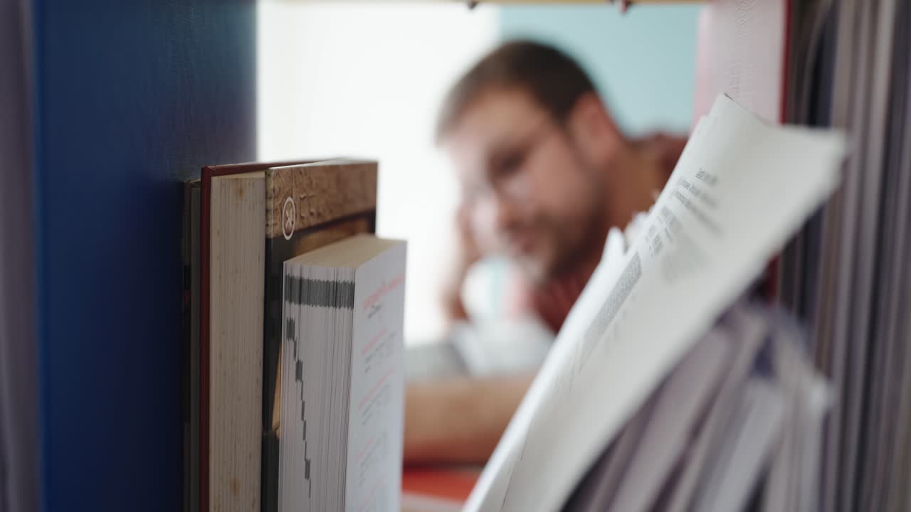 Close-up shot of paperwork and files in focus with a blurred man in the background, highlighting a moment of mental fatigue or deep concentration during study or office work