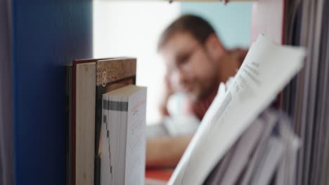 close-up shot of paperwork and files in focus with a blurred man in the background, highlighting a moment of mental fatigue or deep concentration during study or office work