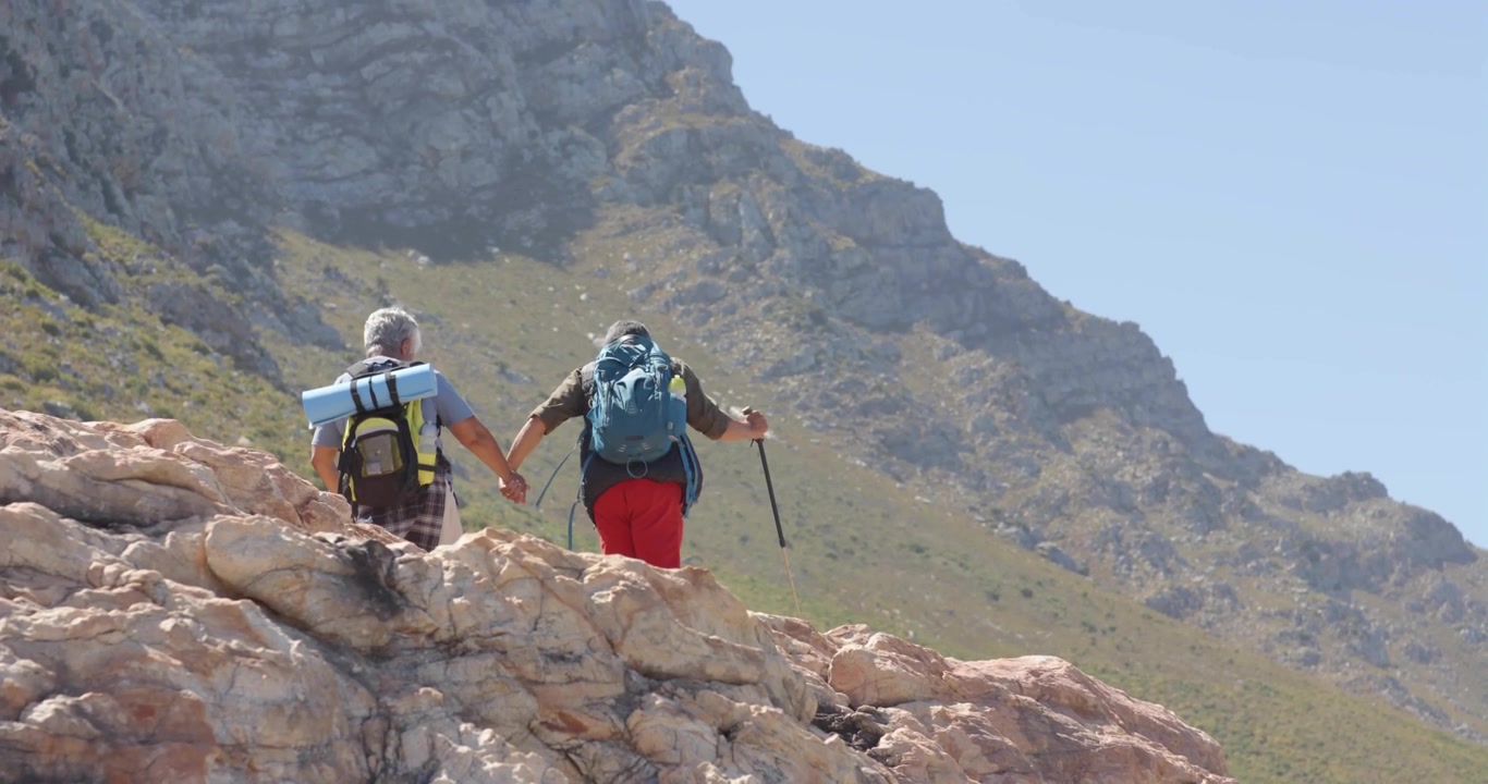 Due escursionisti anziani che salgono su un crinale verso la cima, il titolo "FEEL FREE" che si capovolge rivelando zaini da viaggio