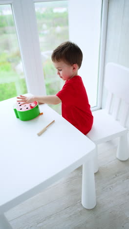 adorable baby boy in red t-shirt sits at desk playing with an educational toy. lovely child having good play time at home. top view. vertical video.