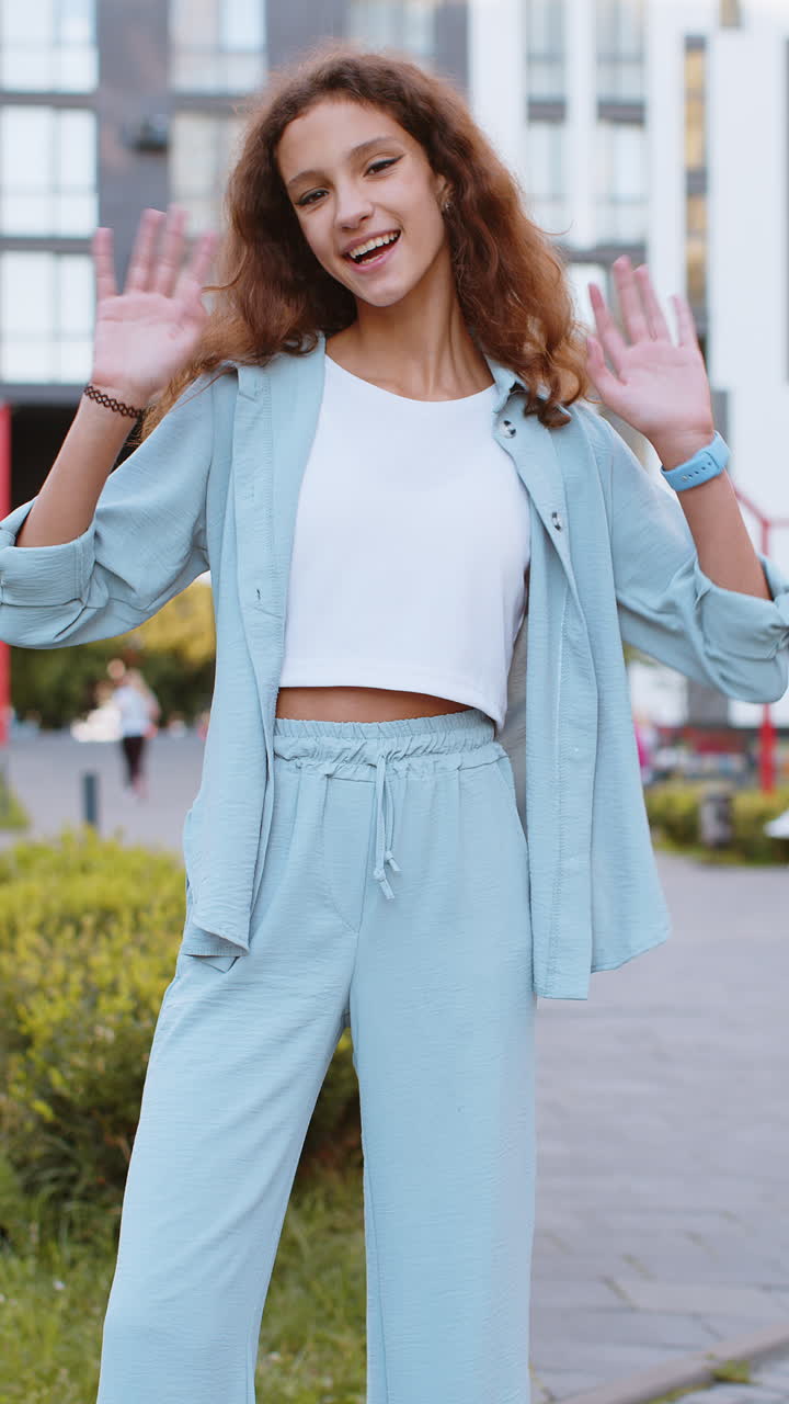 Preteen girl smiling friendly at camera waving hands hello hi greeting or goodbye in city street