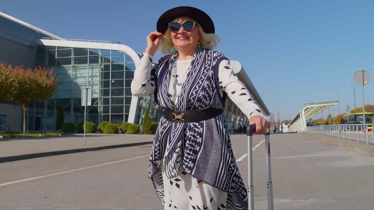 Nonna imprenditrice in pensione che cammina con bagagli nella hall dell'aeroporto, stazione ferroviaria