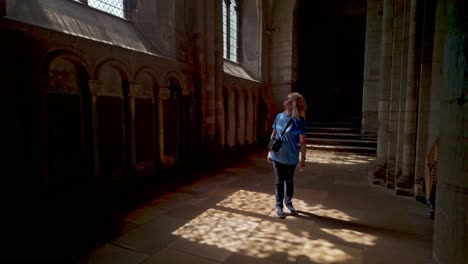 sun light shines through arched church window to female cathedral visitor