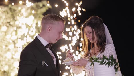 newlyweds eating wedding cake, lovely bride and groom couple cutting dessert with a knife outdoors