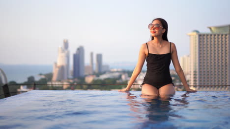 woman relaxing in rooftop infinity pool overlooking city skyline at sunset